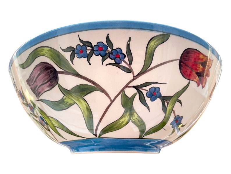 May include: A white ceramic bowl with a blue rim and floral design. The bowl features hand-painted tulips, leaves, and small blue flowers.