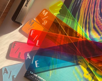 May include: A collection of colorful, transparent record dividers in shades of blue, pink, orange, and green, with etched letters. A black and silver audioquest device and a Tame Impala album are also visible.
