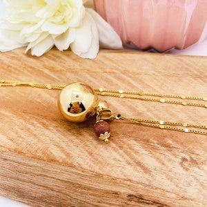 May include: A gold necklace with a large round pendant and a smaller brown stone charm. The necklace is on a wooden surface.