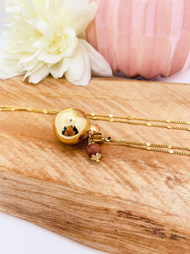 May include: A gold necklace with a large round pendant and a smaller brown stone charm. The necklace is on a wooden surface.