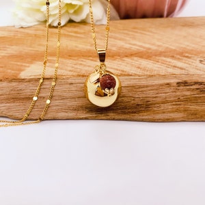 May include: A gold chain necklace with a round gold pendant. The pendant has a small red stone charm attached to it.