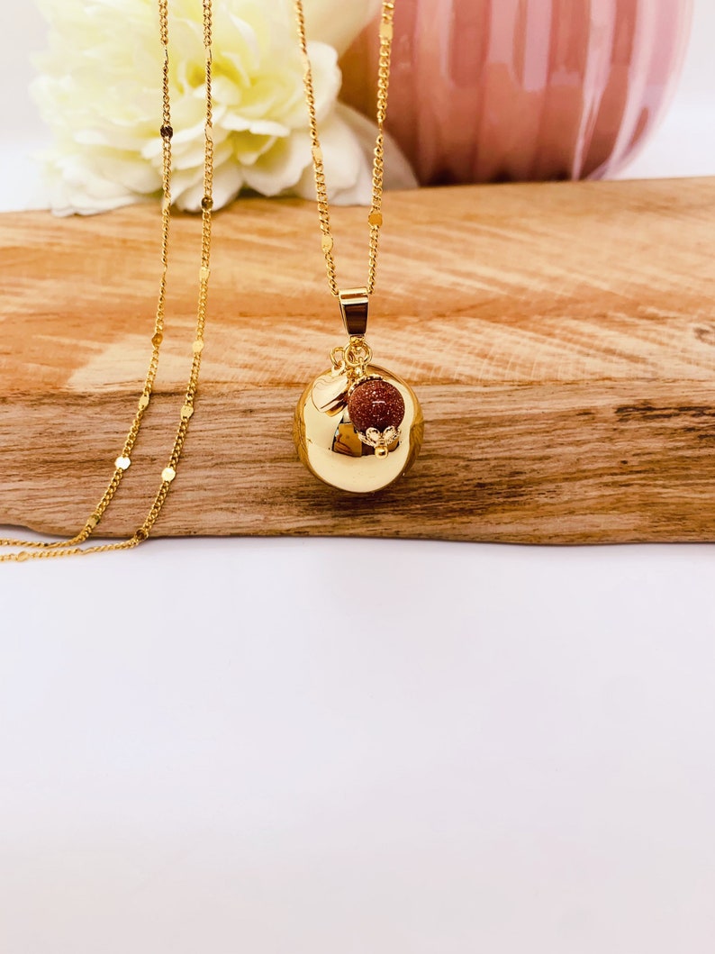 May include: A gold chain necklace with a round gold pendant. The pendant has a small red stone charm attached to it.