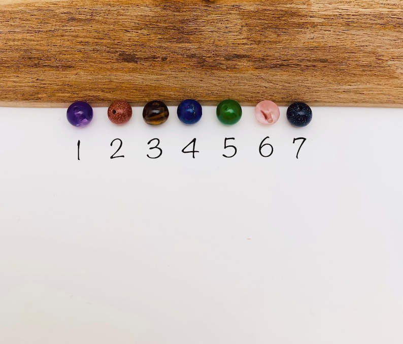 May include: Seven round beads in different colors, numbered 1 through 7. The beads are purple, brown, tiger's eye, blue, green, pink, and dark blue.