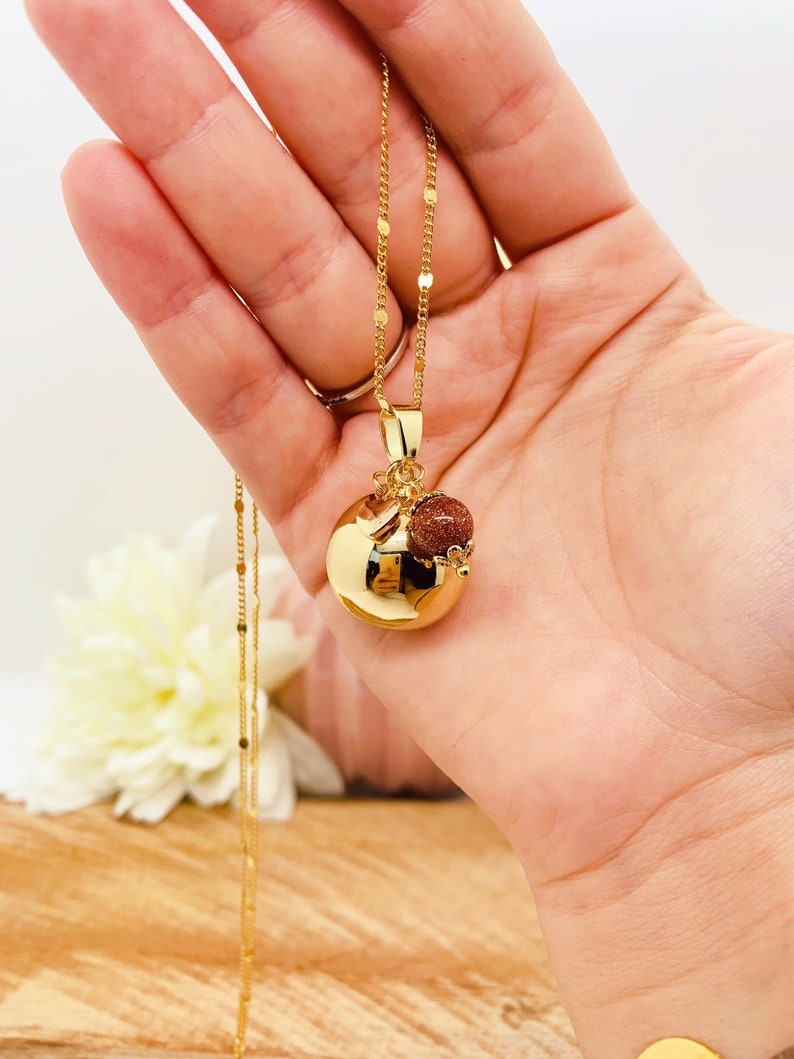 May include: A gold chain necklace with a round gold pendant and a small brown stone charm. The pendant has a textured surface.