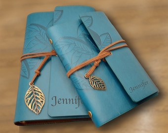 May include: Two blue leather journals with a leaf design and a brown leather strap. The journals have the name "Jennifer" embossed on the front. Each journal has a gold leaf charm attached to the strap.