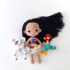 Puede incluir: Mu&ntilde;eca de crochet con el pelo largo y negro, vestida con un vestido marr&oacute;n y naranja, sosteniendo un gallo azul y rojo y un cerdo blanco.