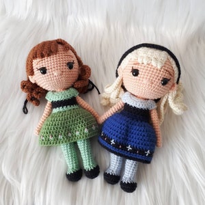 Puede incluir: Dos muñecas de crochet vestidas con vestidos verde y azul. Las muñecas tienen cabello castaño y rubio y ojos negros.