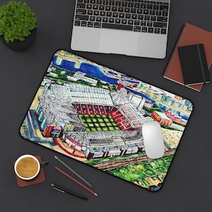 May include: A rectangular mousepad featuring a colorful illustration of a stadium with a red and green field. The artwork includes a detailed depiction of the stadium's architecture, surrounding buildings, and a river. A white mouse sits on the pad.
