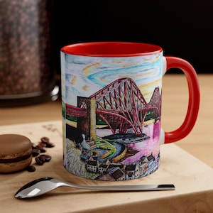 May include: A red and white ceramic mug with a colorful illustration of the Forth Rail Bridge in Scotland. The bridge is depicted in red, yellow, and blue colors against a light blue sky. The mug has a red rim and handle.