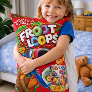 Può includere: Un cuscino rettangolare con il design rosso di una scatola di cereali Kellogg's Froot Loops. La grafica include il logo Froot Loops, Toucan Sam, una ciotola di cereali colorati con latte e il testo Natural Fruit Flavors.
