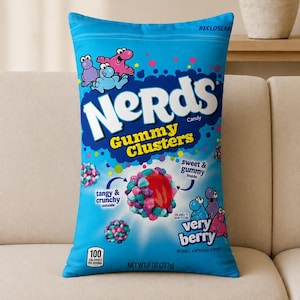 May include: A rectangular throw pillow featuring a bright blue graphic print of a Nerds Gummy Clusters candy bag. The design includes the text Nerds Gummy Clusters, Very Berry, and net weight 8 oz (227g), along with colorful candy illustrations.