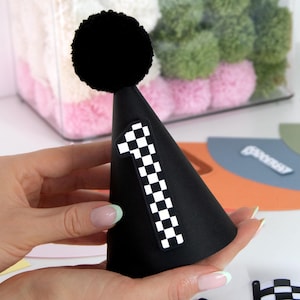 May include: Black party hat with a black pom-pom on top and a checkered number one on the front.