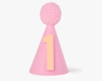 May include: A pink party hat with a light pink pom-pom on top and a light orange number 1 on the front. The hat is cone-shaped and designed for a first birthday celebration.