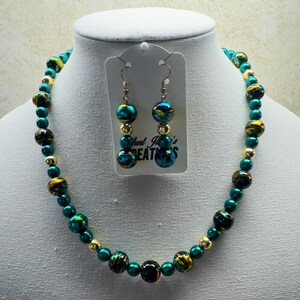 May include: A teal and gold necklace and earrings set. The necklace is made of round beads with a teal base and gold swirls. The earrings are dangle earrings with the same teal and gold beads.
