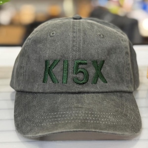 May include: A dark gray baseball cap with a green embroidered logo that says "KI5X".