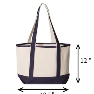 May include: Back view of a canvas tote bag. The bag is cream-colored with navy blue accents on the bottom, top rim, and handles. The tote measures 18.5 inches wide and 12 inches high.