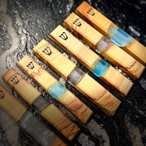 May include: Six wooden mezuzah cases with a blue resin inlay. The cases are made of olive wood and have a crown design carved into the wood.