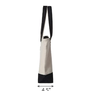 May include: Side view of a canvas tote bag. The bag is primarily beige with a black base and black straps. The base of the bag measures 4.5 inches wide. The text "Side of Tote View" is at the top of the image.