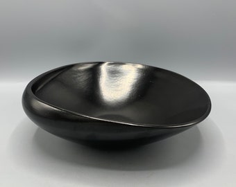 May include: A black ceramic bowl with a rounded, slightly asymmetrical shape. The bowl has a smooth, glossy finish.