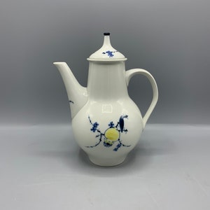May include: A white porcelain coffee pot with a blue and yellow floral design. The pot has a lid and a spout.