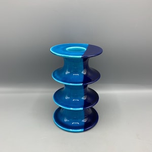 以下が含まれることがあります： 積み重ねられたデザインのセラミックキャンドルホルダー。ホルダーは、明るいティールと濃いネイビーブルーの2つの色セクションに垂直に分割されています。ホルダーは光沢のある仕上げで、円形のトップとベースを備えています。