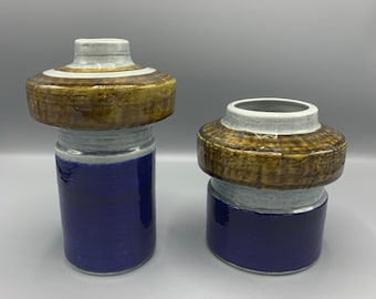 May include: Two ceramic vases with a blue, white and brown geometric design. The vases are cylindrical with a wide, flat top.