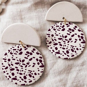 Peut inclure: Une paire de boucles d'oreilles en céramique blanche avec un design en demi-cercle et un design rond avec un motif abstrait noir et blanc.