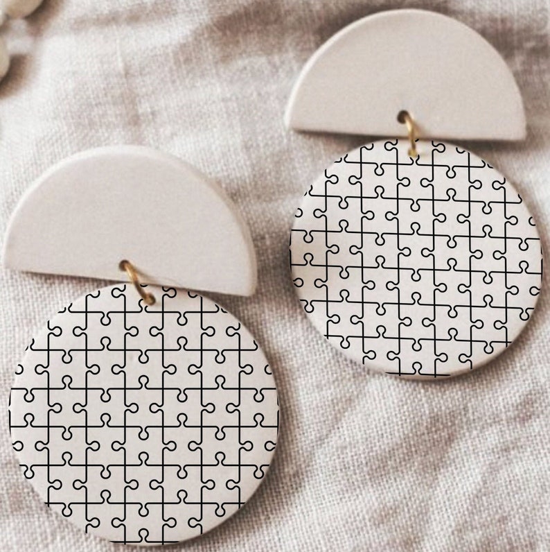 May include: A pair of white ceramic earrings with a half-circle design and a round design featuring a black puzzle piece pattern.