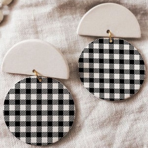 Peut inclure: Une paire de boucles d'oreilles en céramique blanche avec des accents ronds à carreaux noirs et blancs. Les boucles d'oreilles ont la forme d'un demi-cercle avec une petite boucle dorée.