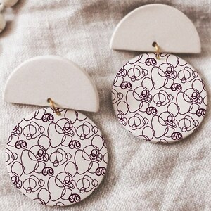 May include: A pair of white ceramic earrings with a half-circle design and a round pendant featuring a black and white abstract pattern.