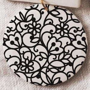 May include: A round, white ornament with a black and white floral pattern. The pattern is intricate and detailed, with swirls and leaves.