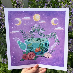 Puede incluir: Una ilustración acuarela púrpura y azul de una tetera con un pez dorado dentro. La tetera está llena de plantas verdes y rodeada de flores. El fondo es un cielo nocturno estrellado con una luna creciente.