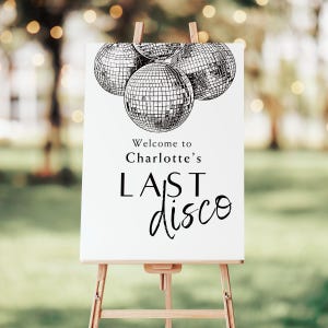 May include: White sign with black text and illustrations of disco balls. The text reads "Welcome to Charlotte's Last Disco".