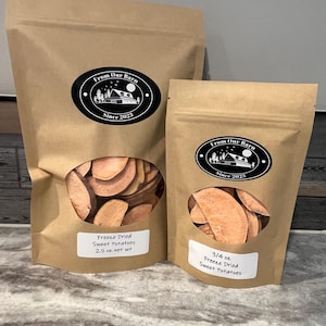 May include: Two brown paper bags of freeze-dried sweet potatoes. The bags have a clear window showing the sliced sweet potatoes. Each bag has a black oval sticker with the text "From Our Barn Since 2023". The larger bag is labeled "2.5 oz net wt". The smaller bag is labeled "3/4 oz".