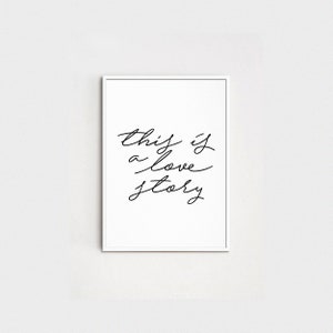 May include: A white framed print with black calligraphy that reads "this is a love story".