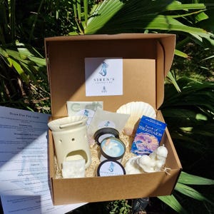 Puede incluir: Una caja de cartón marrón llena de productos del kit de incienso Siren's. La caja contiene un quemador de aceite de cerámica, velas, una concha, una baraja de cartas del tarot y otros artículos. La caja está abierta, revelando el contenido.