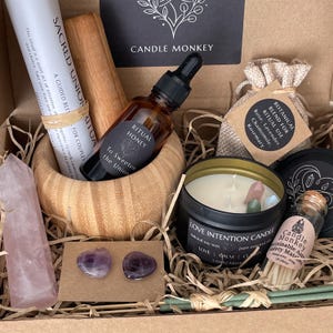 May include: A gift box with various items for a ritual. It includes a candle, essential oil, crystals, matches, a scroll, and a small bag with botanical blend. The box has the text "Candle Monkey" on it.