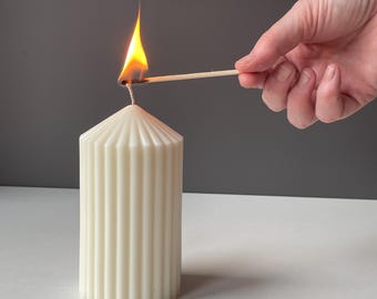 Vela escultórica minimalista, pilar grueso acanalado, estética neutra.