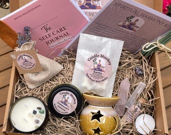 May include: A wellness gift box containing a pink Self Care Journal, a bag of Karma wax melts, a Sandalwood and Patchouli candle with crystals, a yellow star-cutout wax warmer, a lavender sleep pillow, a rose quartz crystal, and incense sticks.