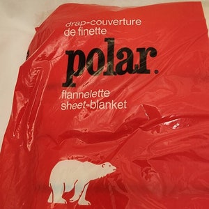 May include: A red plastic package with the word "polar" in large black letters. The package also has the words "drap-couverture de finette" and "flannelette sheet-blanket" in white text. A white polar bear graphic is on the bottom.