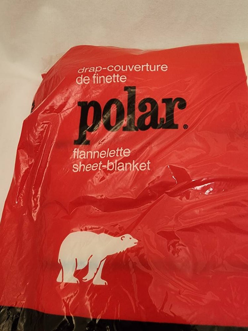 May include: A red plastic package with the word "polar" in large black letters. The package also has the words "drap-couverture de finette" and "flannelette sheet-blanket" in white text. A white polar bear graphic is on the bottom.