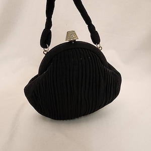 Cartera negra Art Deco, cierre ornamentado, asa corta.