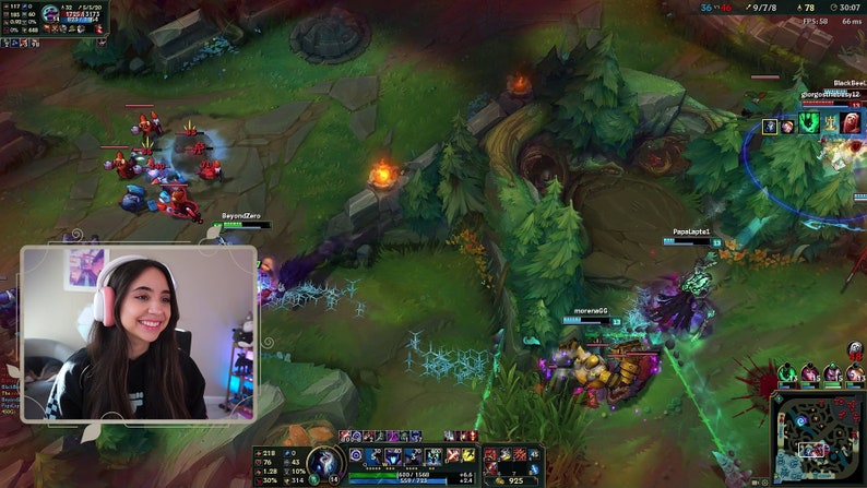 Puede incluir: Una mujer con auriculares sonr&iacute;e mientras mira un videojuego en la pantalla de una computadora. El juego es League of Legends, y la pantalla muestra una pelea de equipo en la jungla. La mujer lleva una camisa blanca y negra y tiene el pelo largo y casta&ntilde;o.