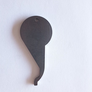 Puede incluir: Un abridor de botellas de metal gris oscuro con forma de llave. Tiene una parte superior circular con un agujero, un cuerpo en forma de lágrima y un gancho curvo en la parte inferior. El abridor está sobre un fondo blanco.