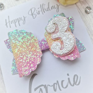 May include: A rainbow glitter bow with a white glitter number 3 on top. The bow is on a white card with the text "Happy Birthday Gracie".