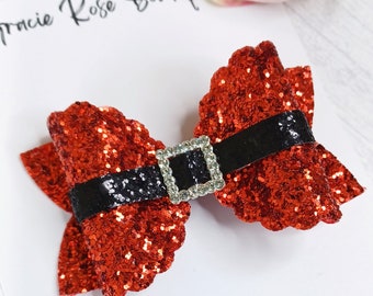 May include: Red glitter bow with a black belt and a rhinestone buckle. The bow is a Christmas-themed hair accessory.