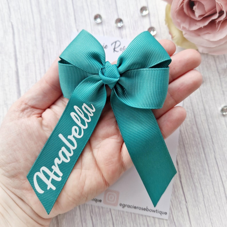 May include: Teal ribbon bow with the name "Arabella" written in white on the ribbon.