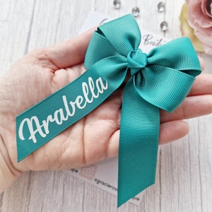 May include: A teal blue ribbon bow with a white personalized name tag that says "Arabella".