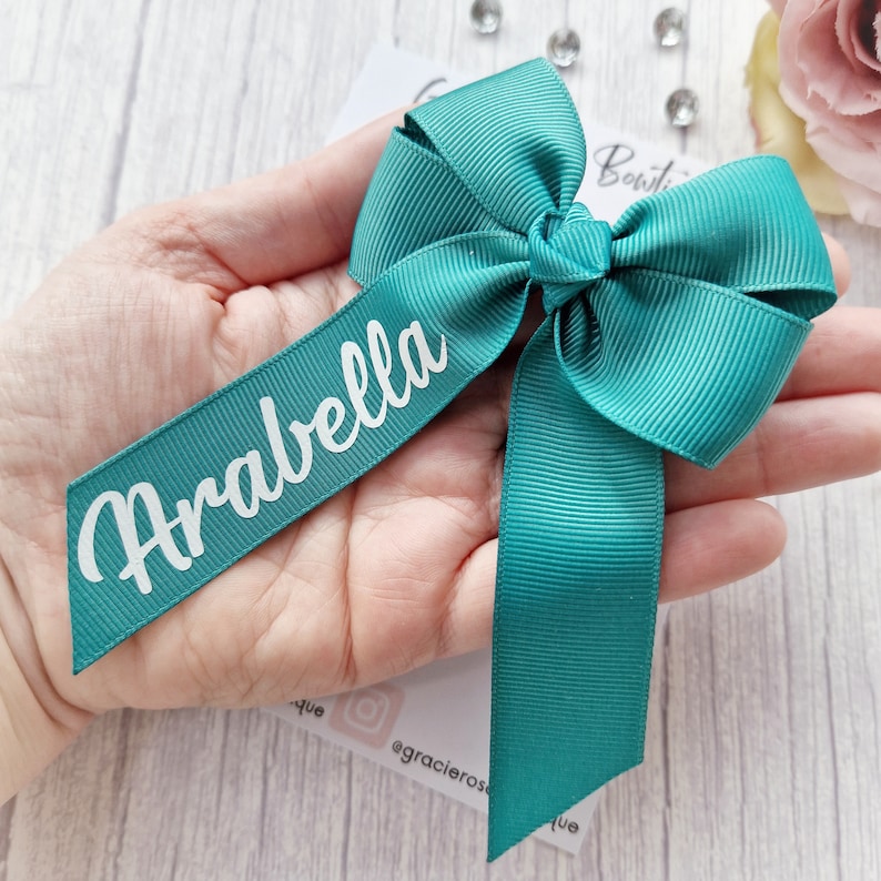 May include: A teal blue ribbon bow with a white personalized name tag that says "Arabella".