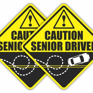 May include: Two yellow caution signs with black borders and a white exclamation point inside a black triangle. The signs read "CAUTION SENIOR DRIVER" with a black car and a white dashed line representing a car swerving.